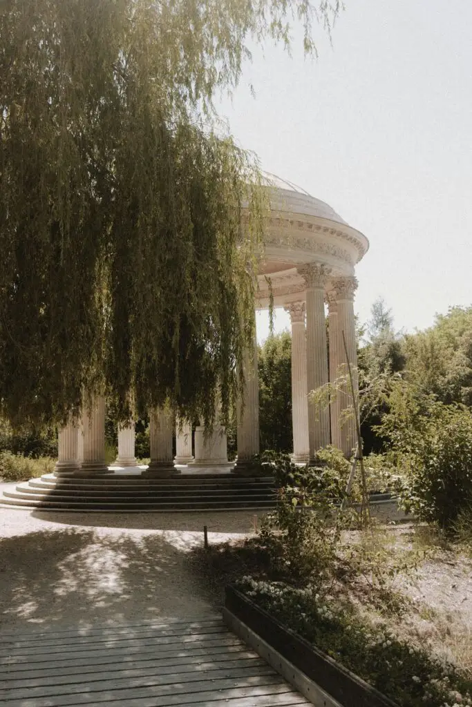 Romantic Versailles scene featuring the Temple of Love partially covered by a graceful weeping willow in a serene garden setting.