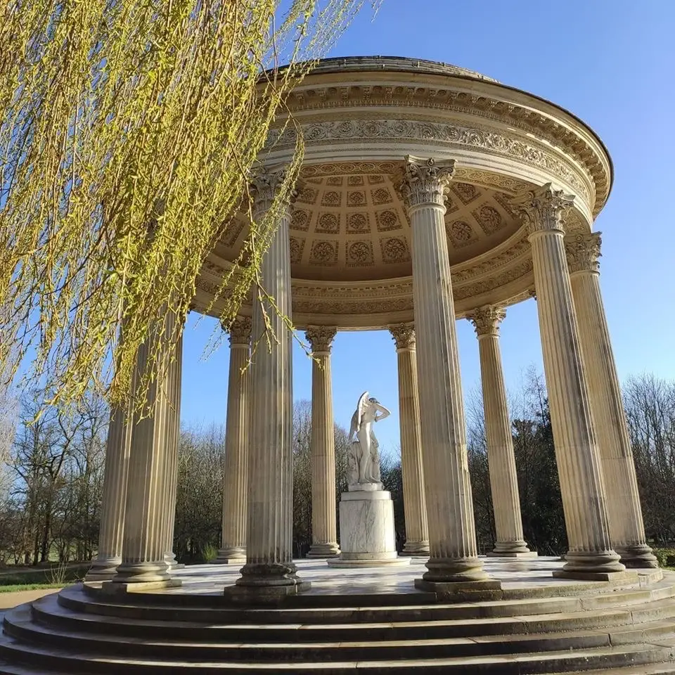 Romantic Versailles landmark featuring the Temple of Love with classical columns, ornate dome, and a statue of Cupid beneath a clear blue sky.