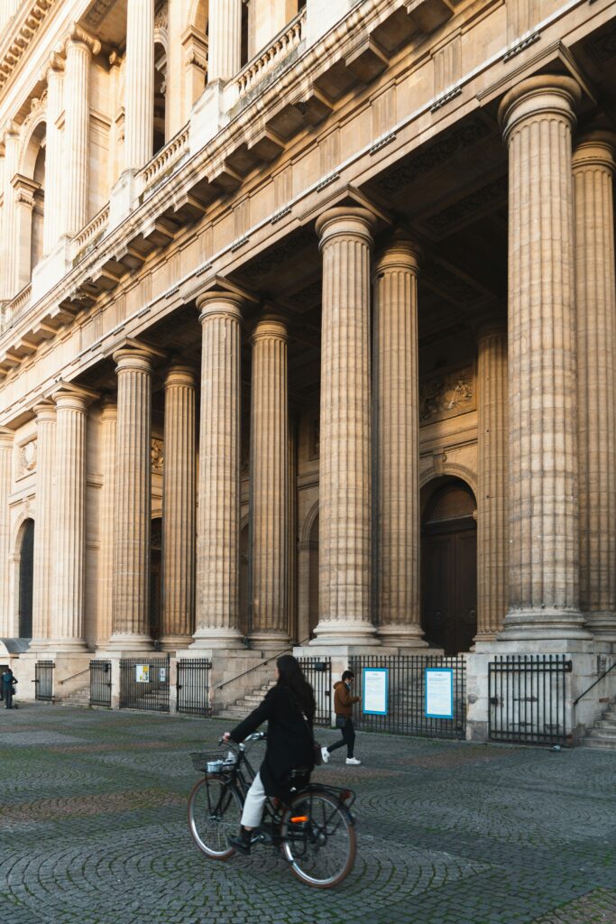 Lady on bike, cycling around paris in front of grand pillars.
