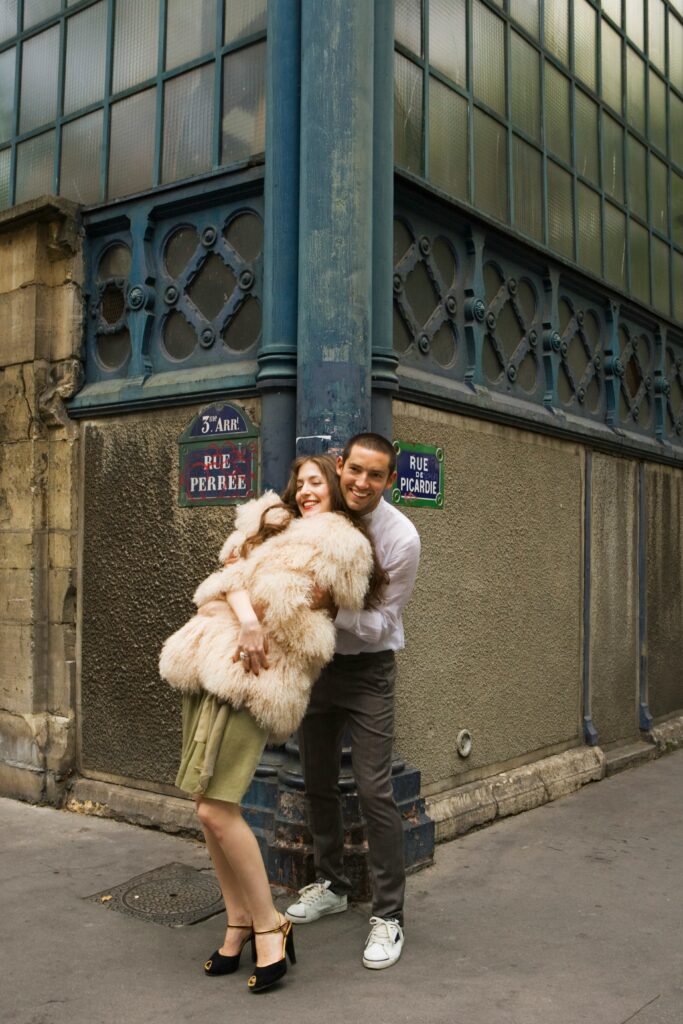 Smiling couple embracing on a Paris street corner in the Marais district, near Rue Perrée and Rue de Picardie.