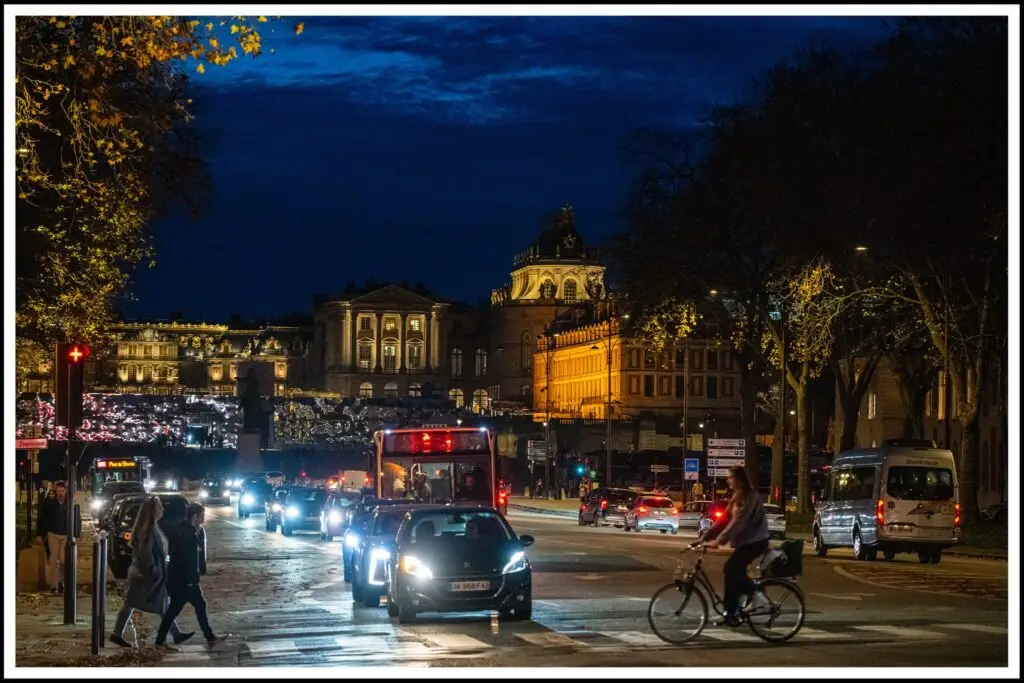 Night traffic and busy parking near the Palace of Versailles, with cars, buses, and bicycles at Place d'Armes – a prime parking Versailles location for palace visitors.