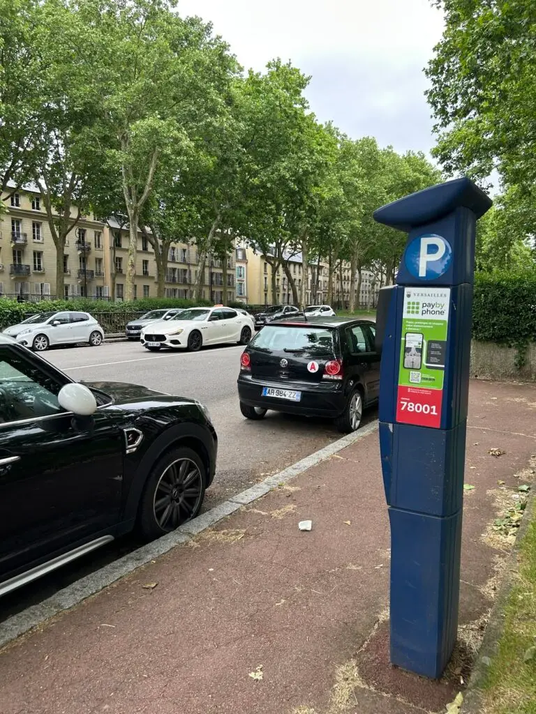 Street parking in Versailles with a 'PayByPhone' meter in the foreground and cars parked under a canopy of leafy trees along a residential street.