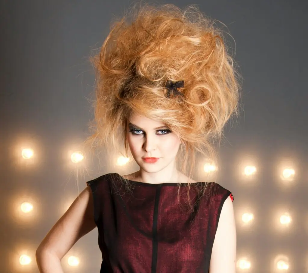 Marie Antoinette hair inspo featuring a teased, voluminous updo with a modern edge and no visible curls, styled with a dramatic hair bow.
