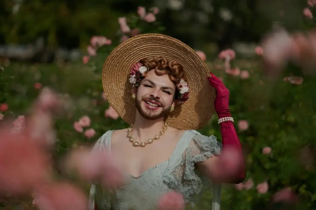 Marie Antoinette hair inspo with a whimsical modern twist—vintage-inspired curls adorned with flowers and berries, paired with a wide-brimmed straw hat, pearls, and Rococo-style lace dress in a blooming rose garden.