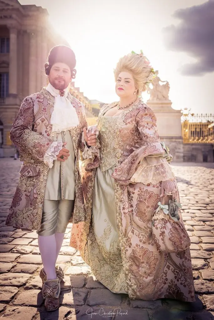 Couple in coordinated rococo costumes at Versailles, wearing gold and rose brocade with lace trims and powdered hairstyles